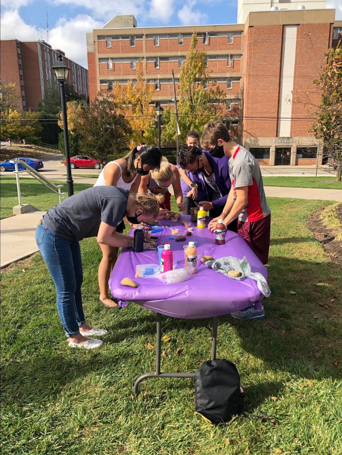 Group of students painting rocks on a table outside